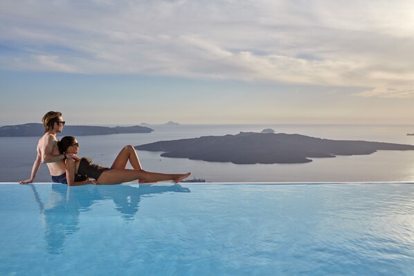 Una pareja relajándose junto a una piscina con una vista panorámica del océano y las islas.