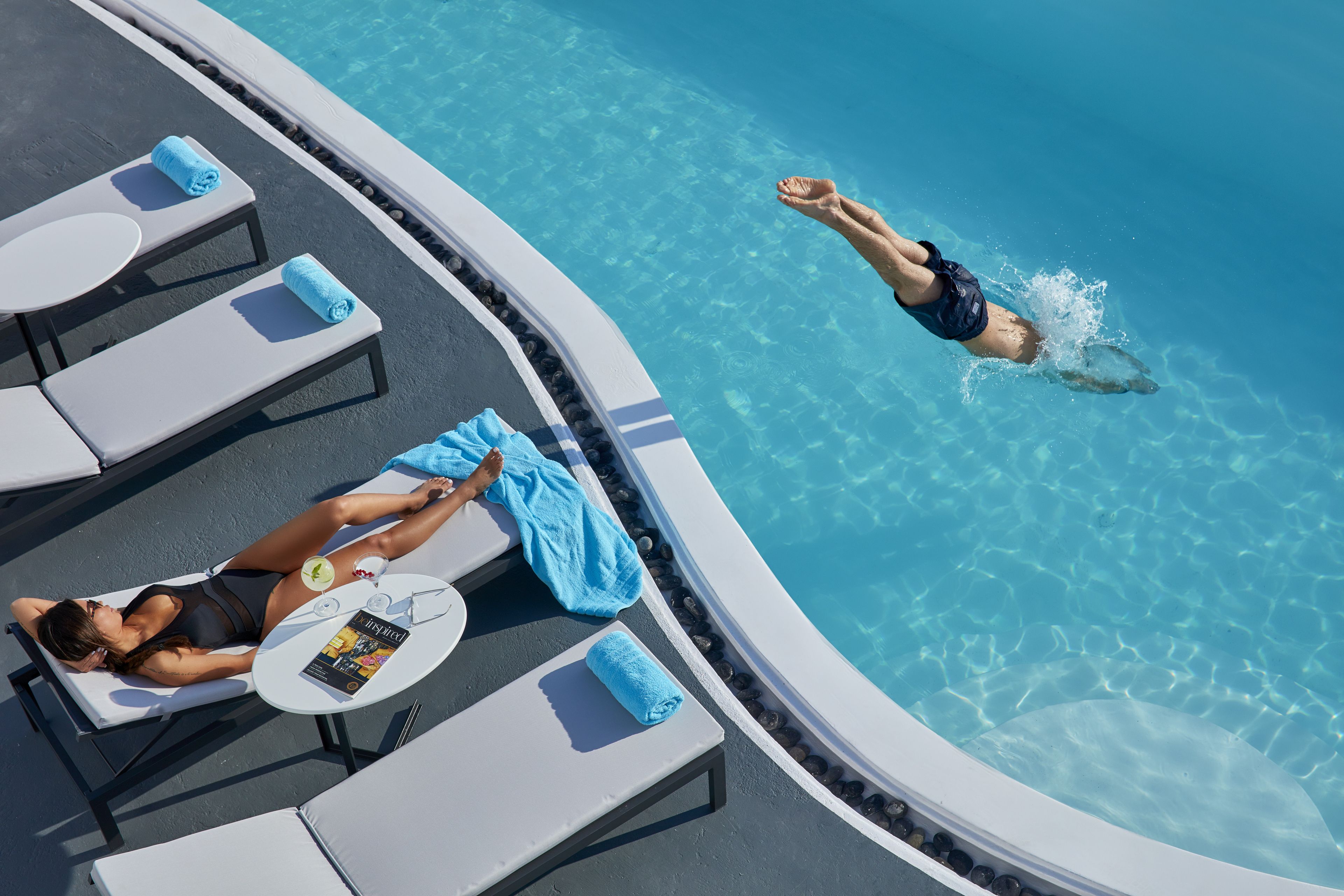 Área de piscina com espreguiçadeiras e alguém nadando.