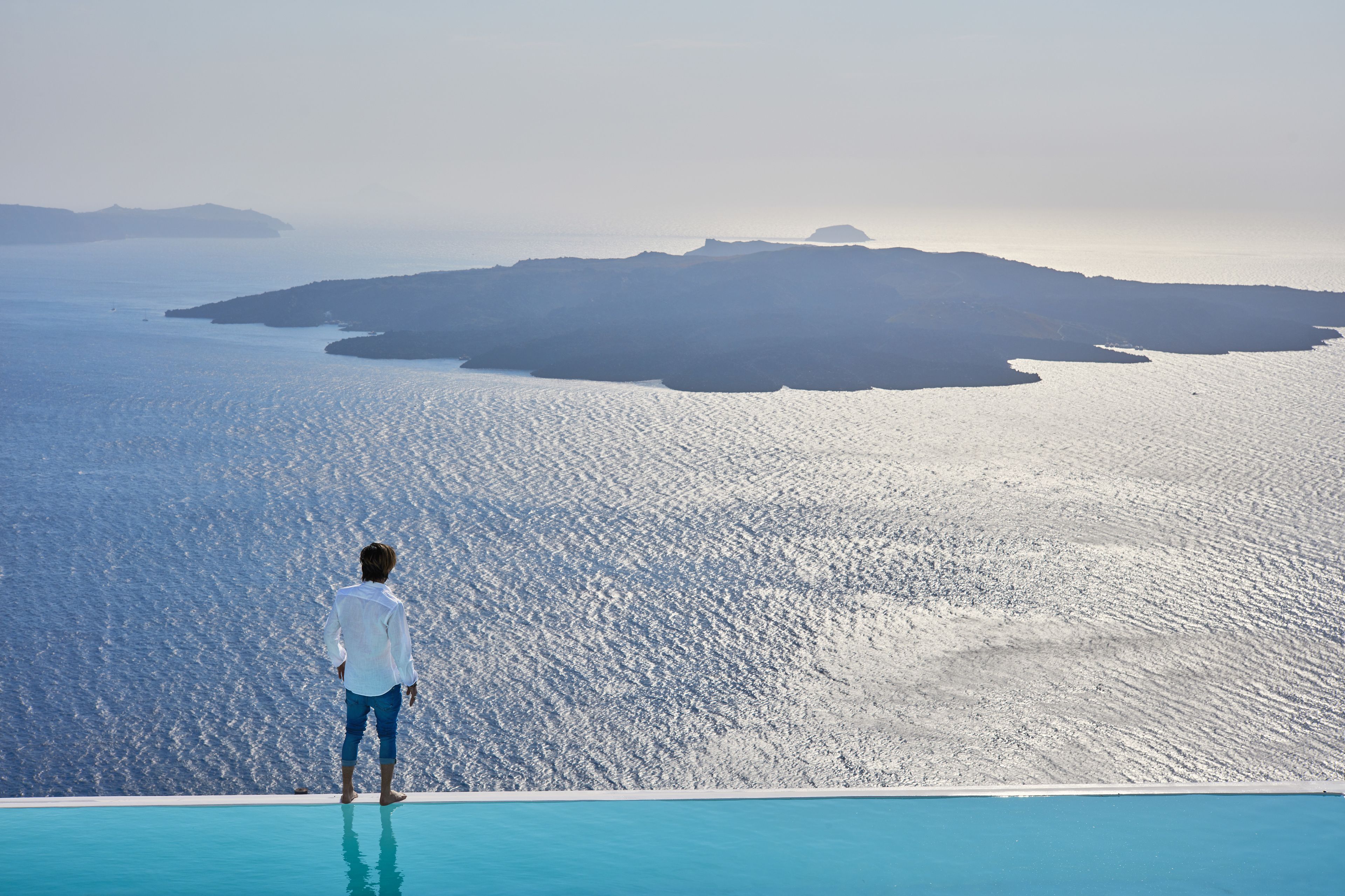 A person standing at the edge of a pool overlooking a large body of water with distant landforms.