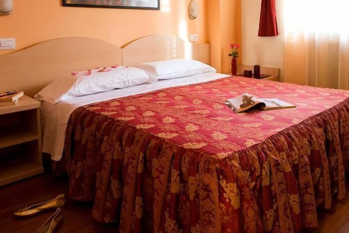 A hotel room with a bed, a nightstand, a bedside table, and a window with curtains.