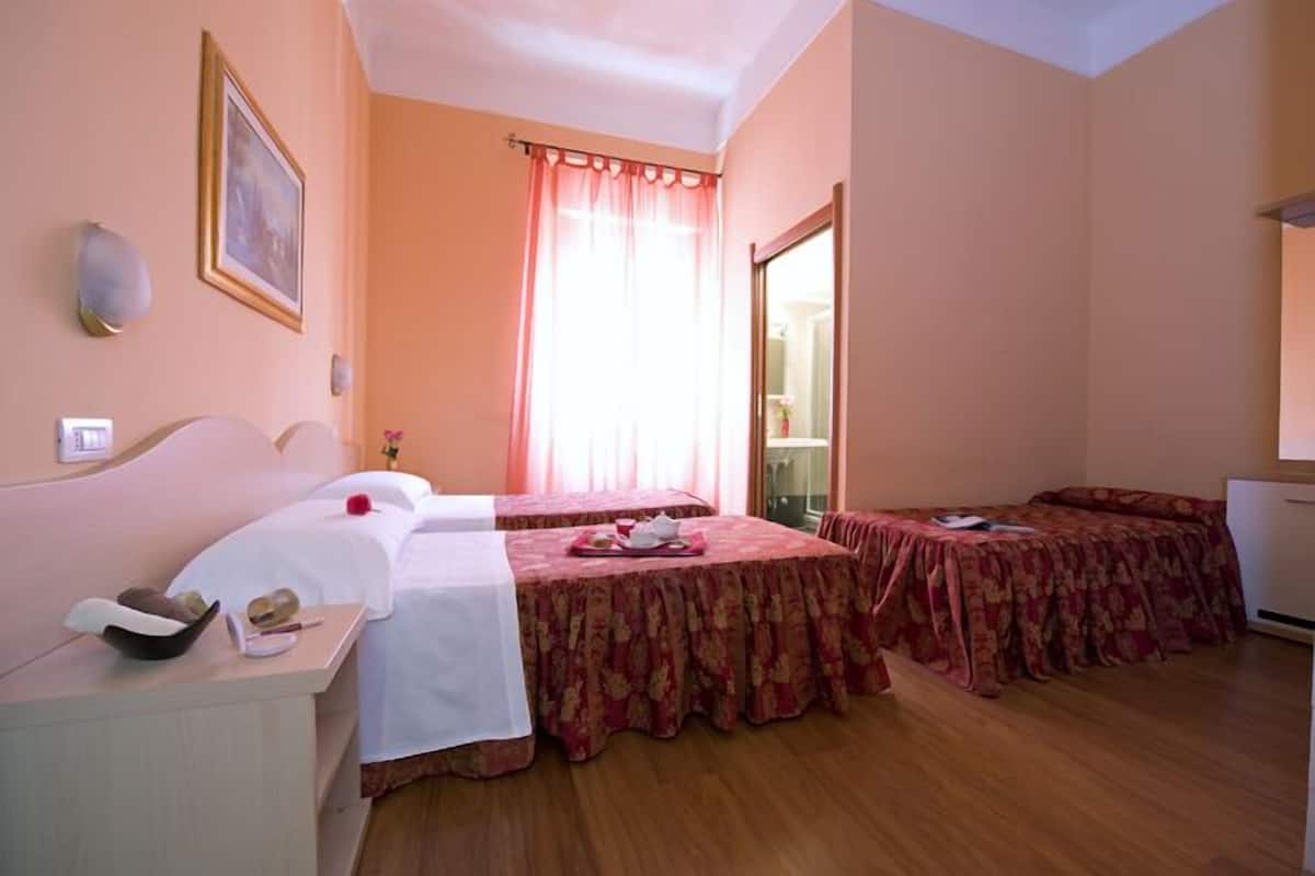 A hotel room with two beds, a small table, a mirror, and a window with curtains.