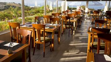 A restaurant with wooden tables and chairs, large windows, and umbrellas.