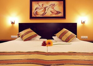 Habitación de hotel con una cama grande, dos almohadas, una obra de arte enmarcada sobre la cama y dos lámparas fijadas a la pared.