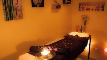 A room with a massage table, a candle, and a vase with flowers.