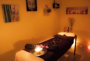 Una habitación con una camilla de masaje, una vela y un jarrón con flores.