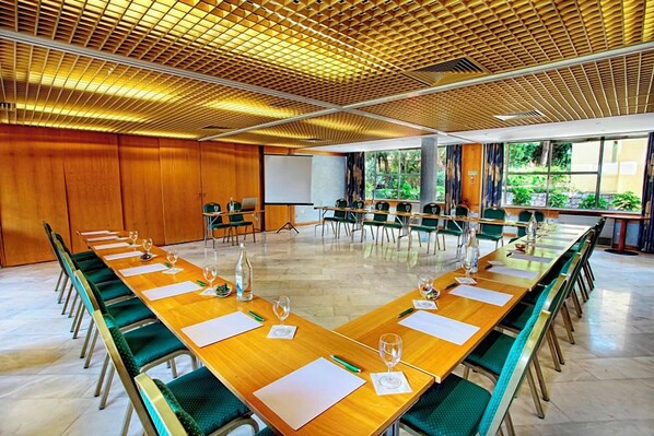 Un salón de conferencias con una larga mesa, sillas, una pantalla de proyector y vistas a zonas verdes.