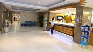 A hotel reception area with a reception desk, a TV, a blue seating area, and a plant. - Baia Cristal Beach & Spa Resort (Lagoa)