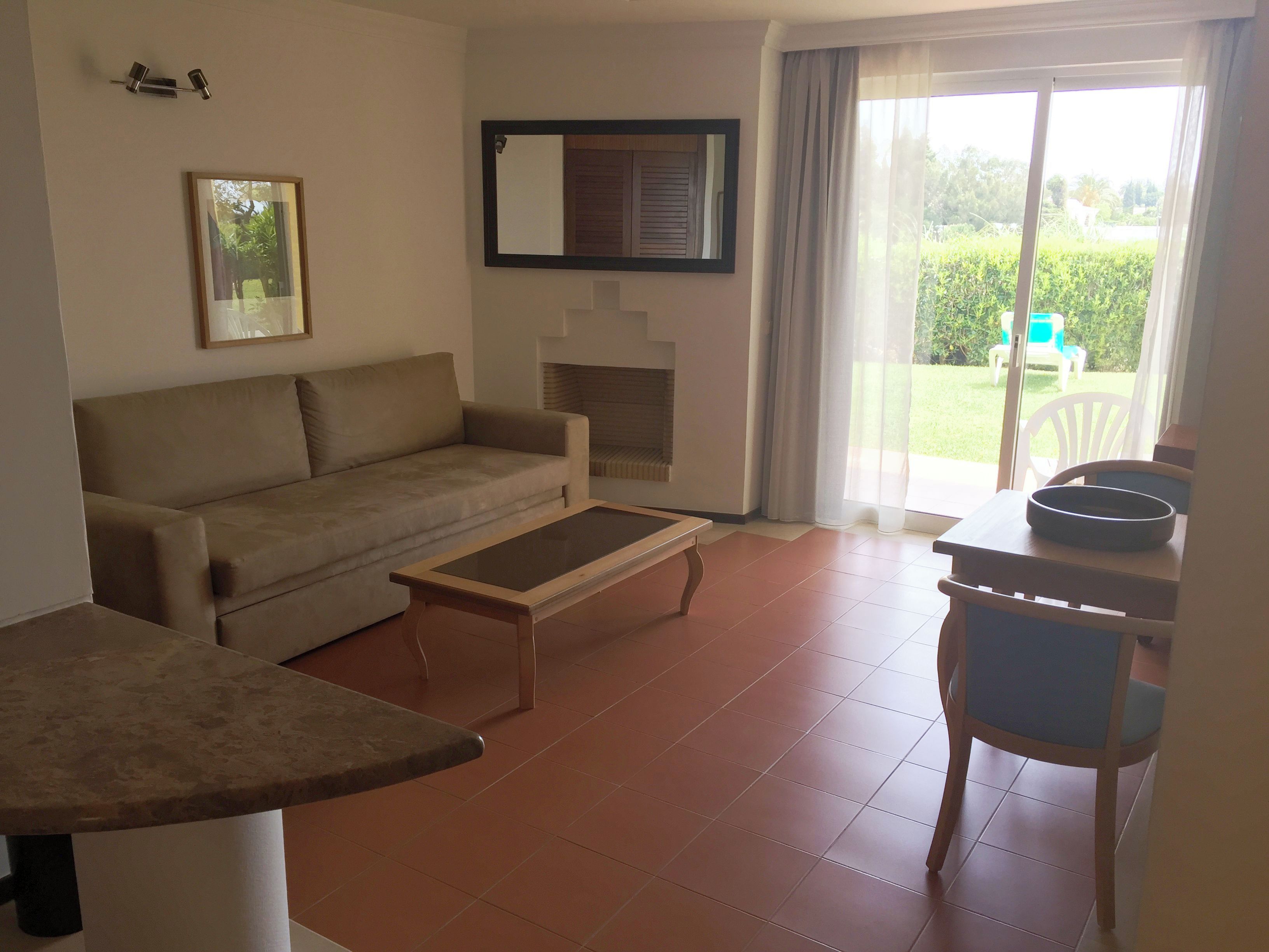 A living room with a sofa, coffee table, and a fireplace. There is a dining area with a table and chairs.