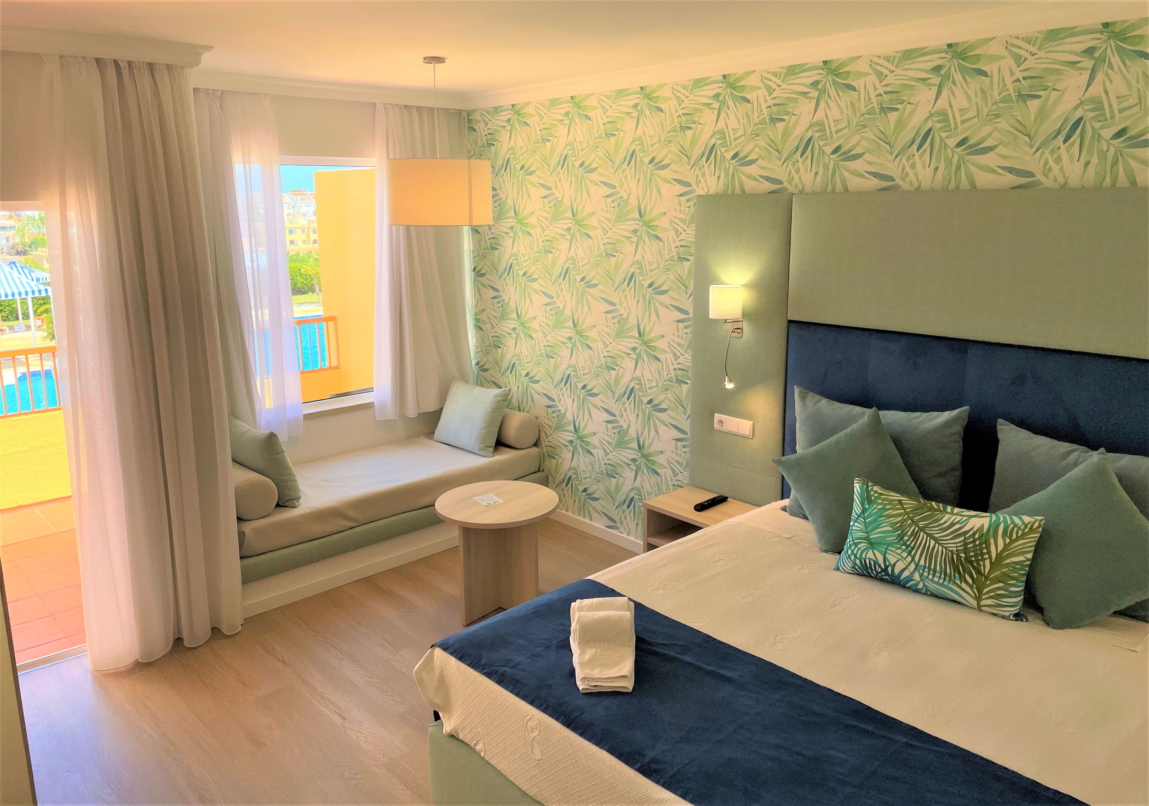 A hotel room with a bed, a sofa, a small table, and a window with curtains.