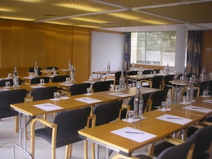 Un salón de conferencias con mesas, sillas, botellas de agua y una pantalla de proyector.