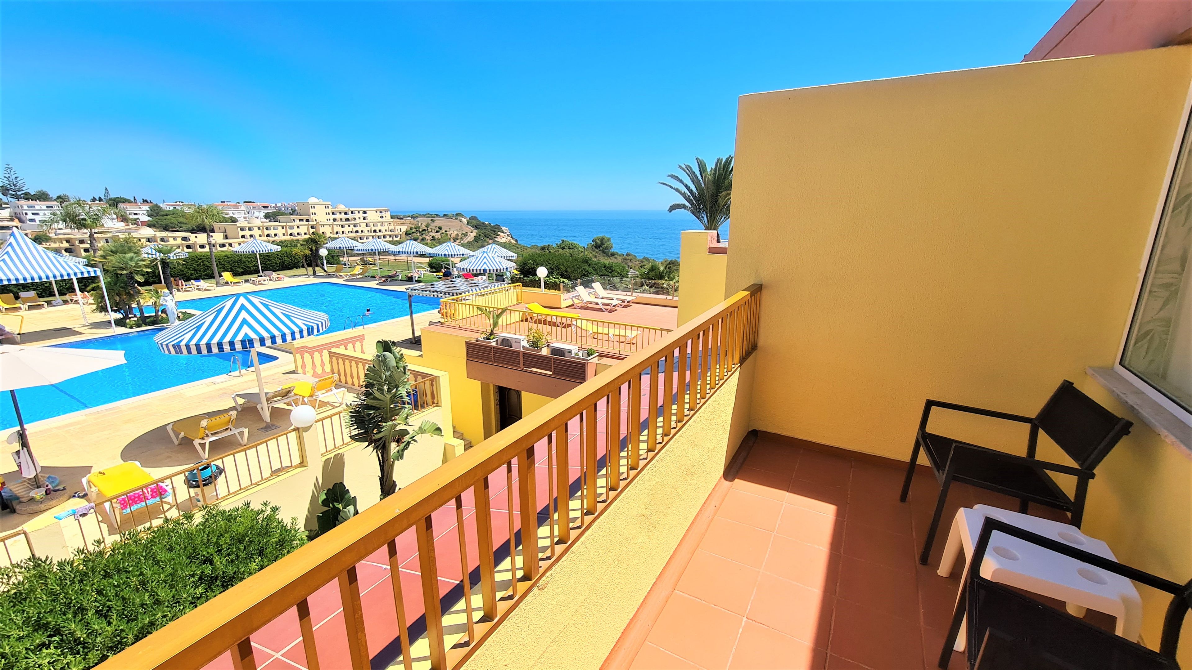 Ein Balkon mit Blick auf einen Pool und Strandstühle, ein Stuhl und ein Tisch.