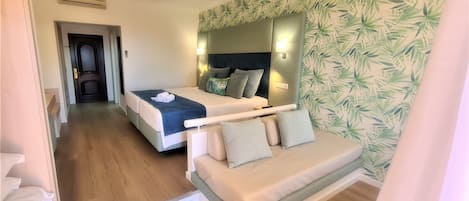 A hotel room with a bed, a sofa, a mirror, and a wall with a leaf pattern.