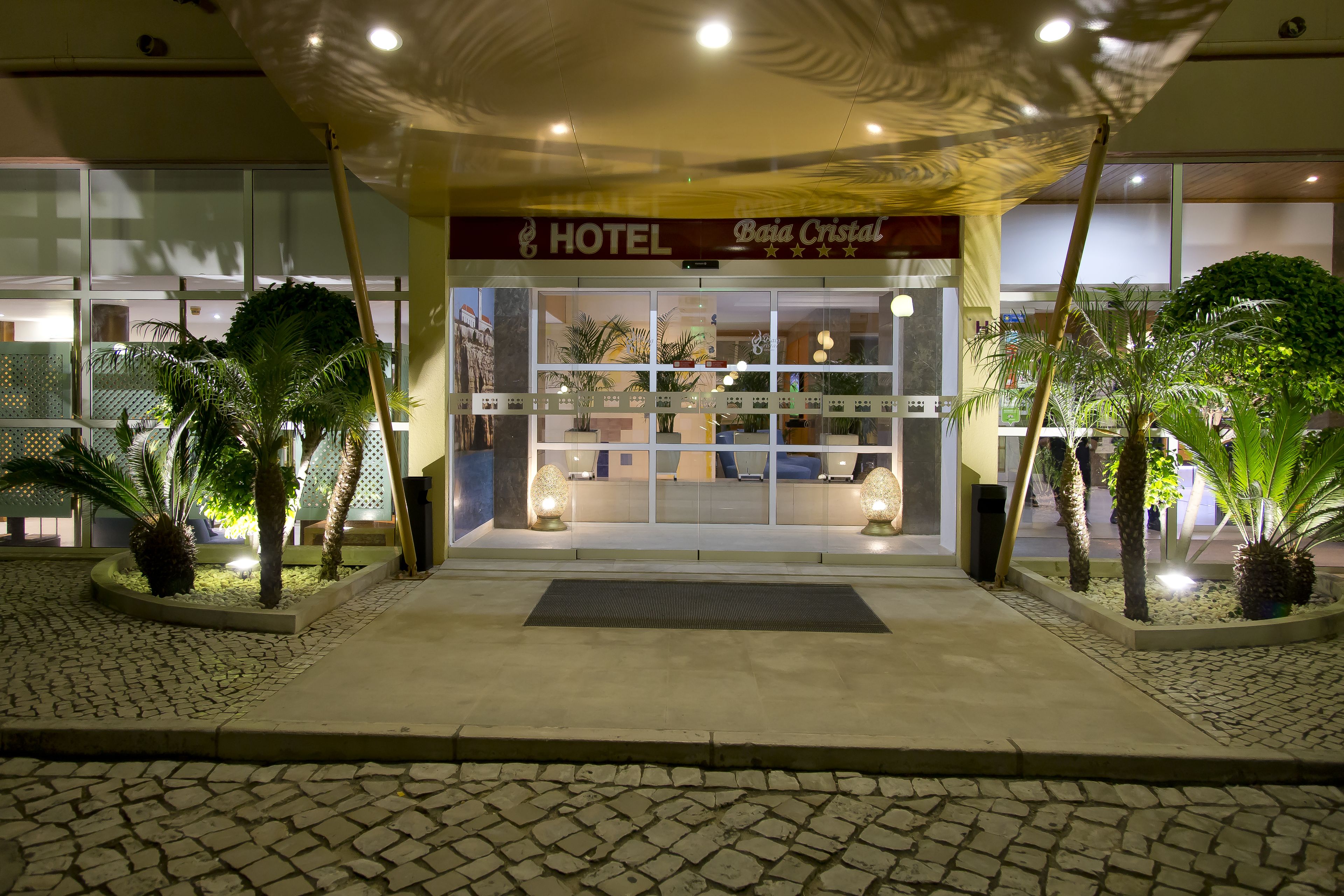 A hotel entrance with a sign reading 'HOTEL Boa Cristal,' a tiled pavement, and potted plants.