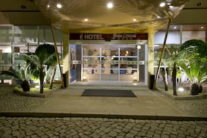 Entrada de un hotel con un cartel que dice 'HOTEL Boa Cristal', pavimento de baldosas y plantas en macetas.