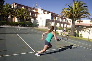 Una cancha de tenis con red, palmeras y un edificio al fondo.