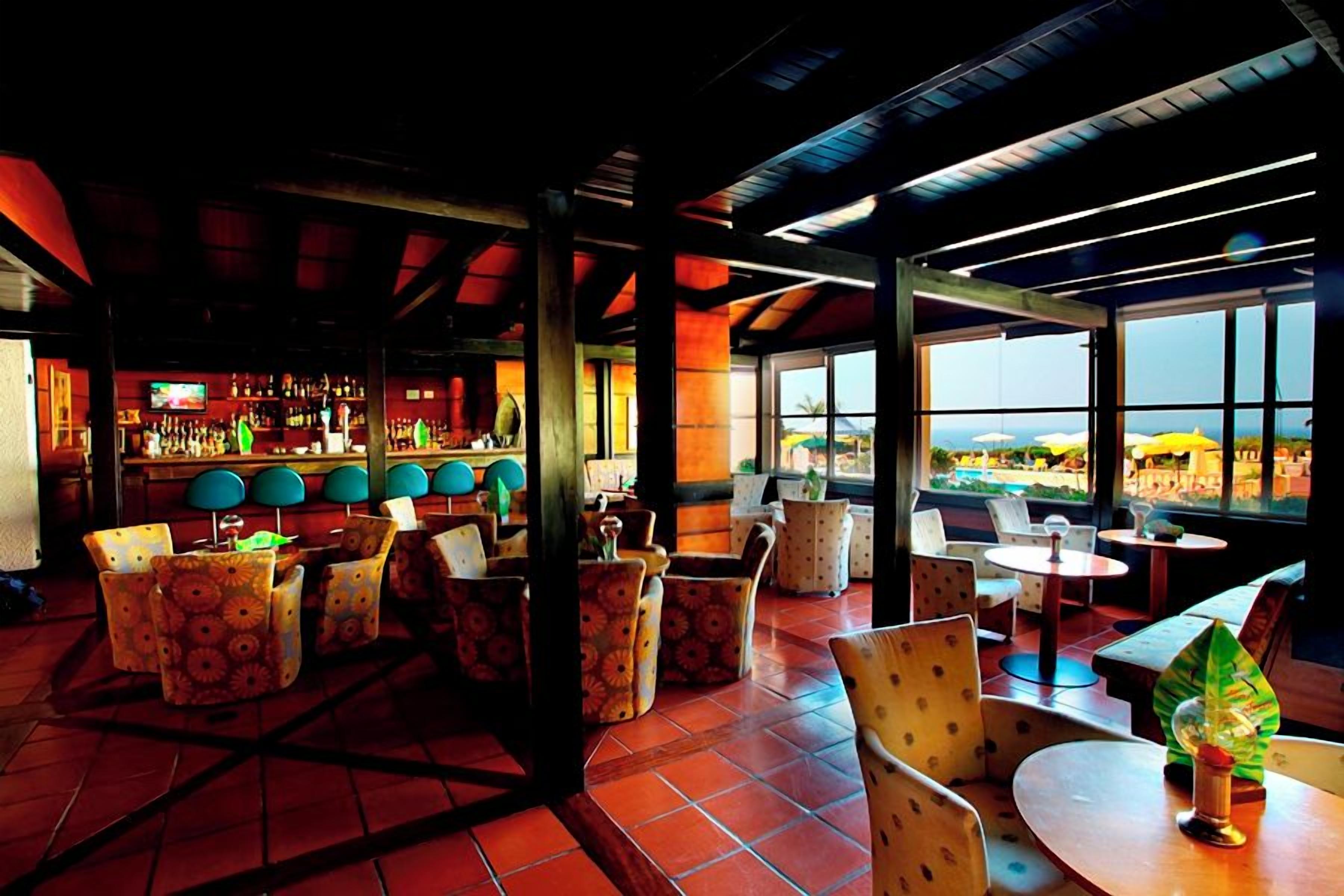 A restaurant with a bar area, outdoor seating, and large windows offering a view.