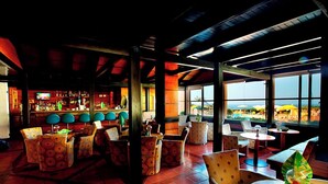A restaurant with a bar area, outdoor seating, and large windows offering a view. - Baia Cristal Beach & Spa Resort (Lagoa)