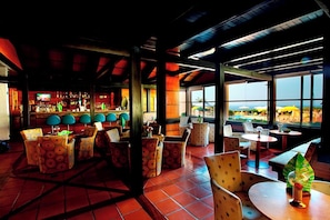 Un restaurante con zona de bar, mesas al aire libre y grandes ventanales con vistas.