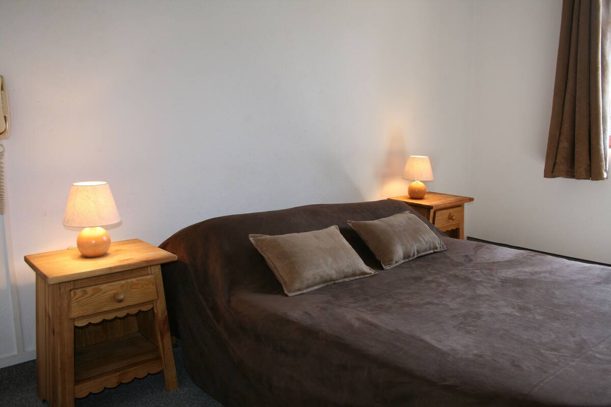 A bedroom with a bed, two bedside tables, a lamp on each table, and a curtain on the window.
