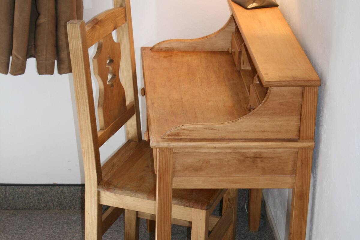 A wooden desk with a lamp, a chair, and a window with curtains.