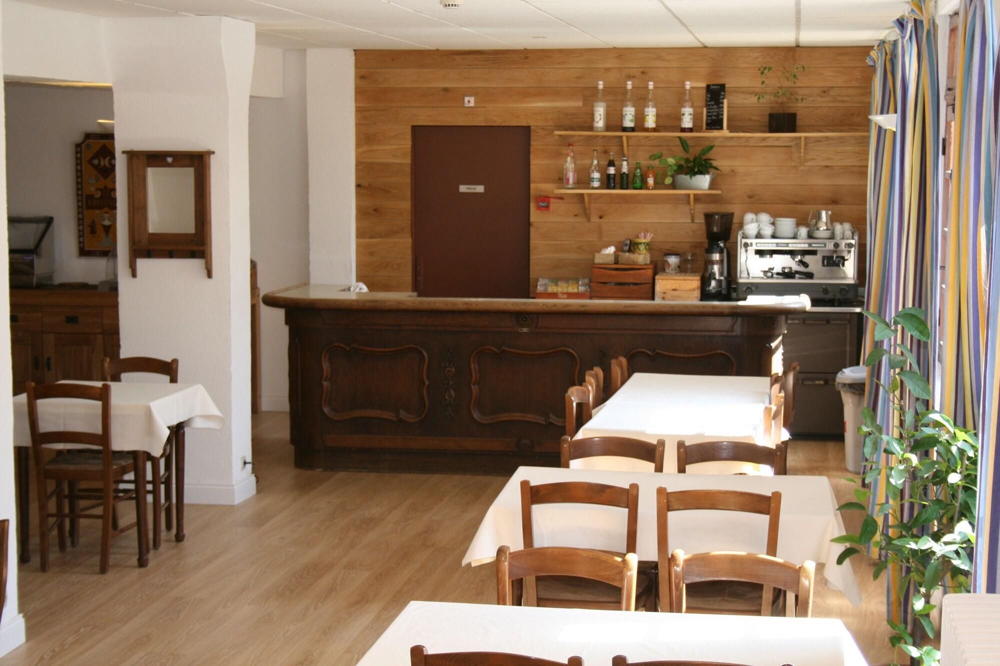 Un coin repas avec des tables et des chaises en bois, une cuisine avec des armoires et des étagères en bois, et un rideau à rayures.