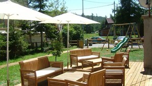 An outdoor patio with wooden furniture, including sofas and tables, and a swing set in the background. - Adonis Le Chastellan (Guillaumes)