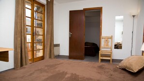 A bedroom with a large bed, a wooden chair, a wooden wardrobe, and a mirror on the wall. - Adonis Le Chastellan (Guillaumes)