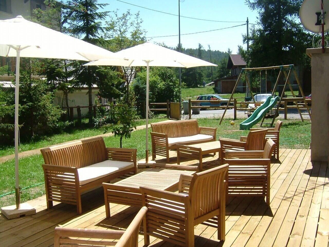 An outdoor patio with wooden furniture, including sofas and chairs, and a swing set in the background.