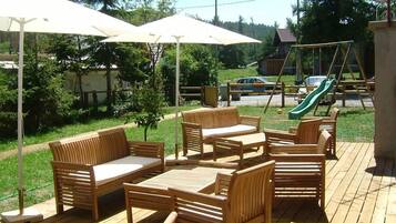 An outdoor patio with wooden furniture, including sofas and chairs, and a swing set in the background.