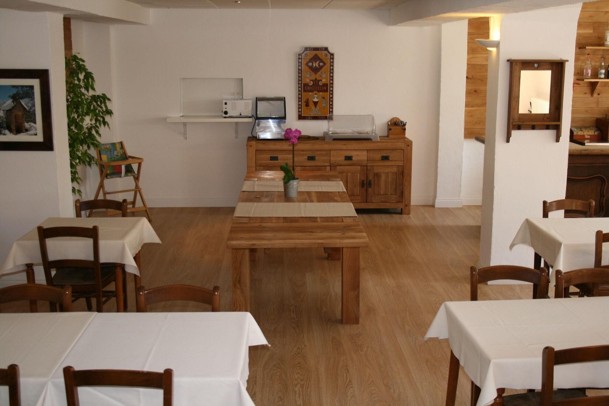 A dining area with wooden tables and chairs, a kitchen area with cabinets and appliances, and a wall-mounted clock.