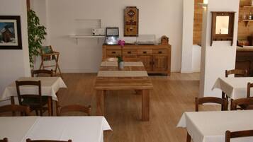 A dining area with wooden tables and chairs, a kitchen area with cabinets and appliances, and a wall-mounted clock.