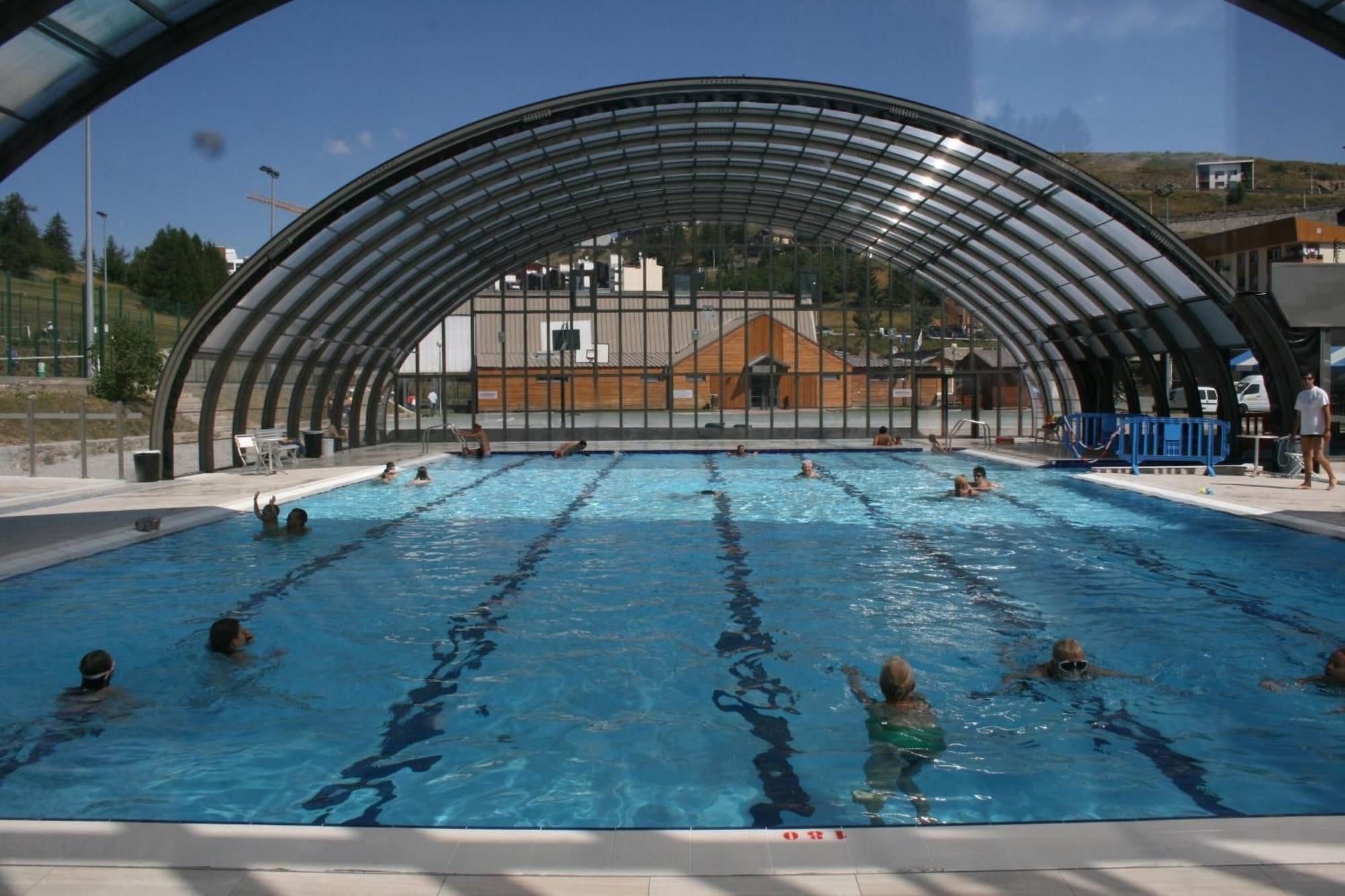 Une piscine intérieure dotée d’une structure de toit incurvée, de couloirs de nage bien délimités et offrant une vue sur les bâtiments en arrière-plan.