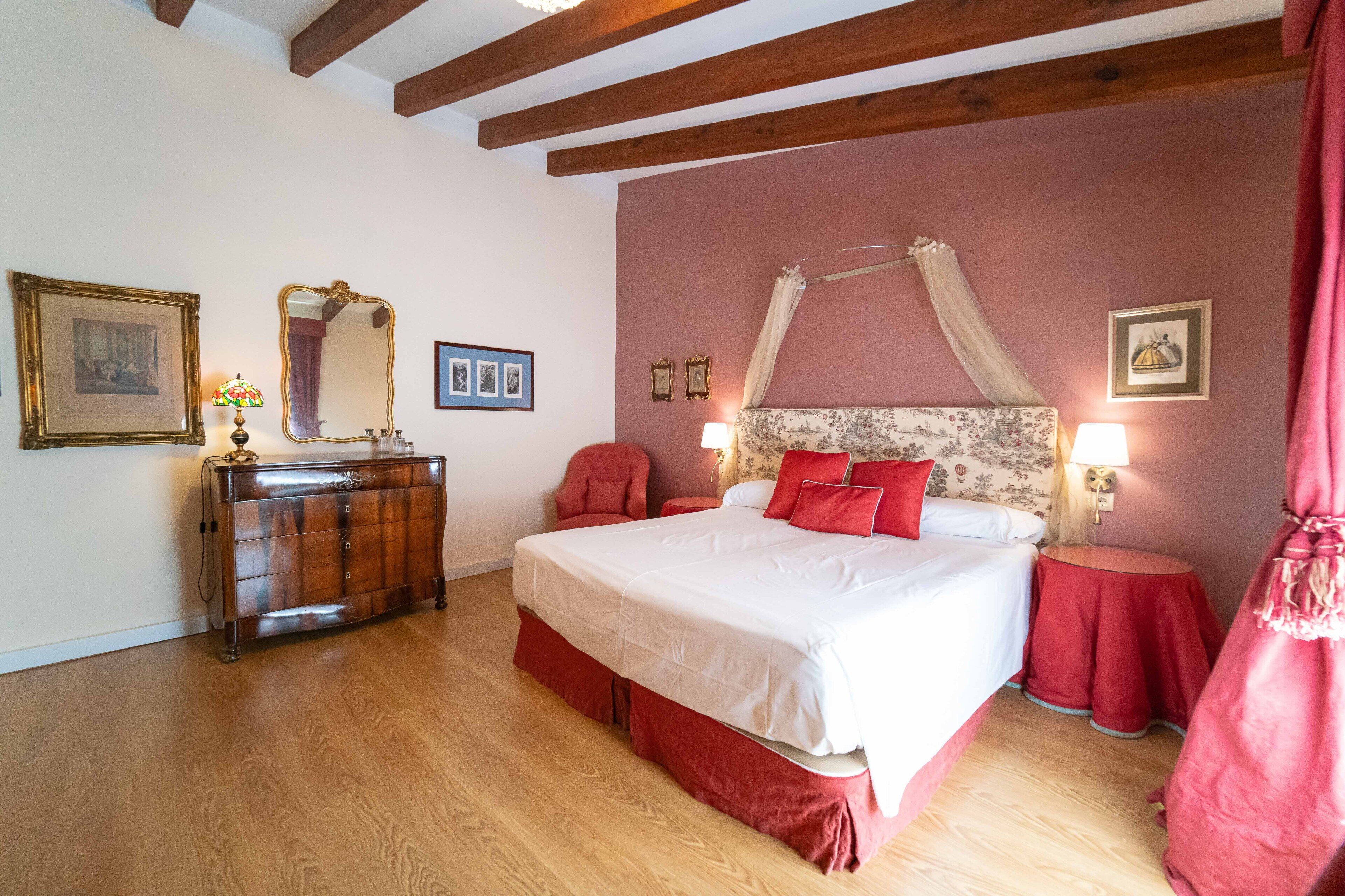 A bedroom with a large bed, a wooden dresser, a mirror, and a red curtain.
