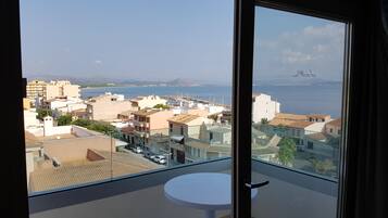 A balcony with a table, overlooking a coastal town with buildings and a marina.