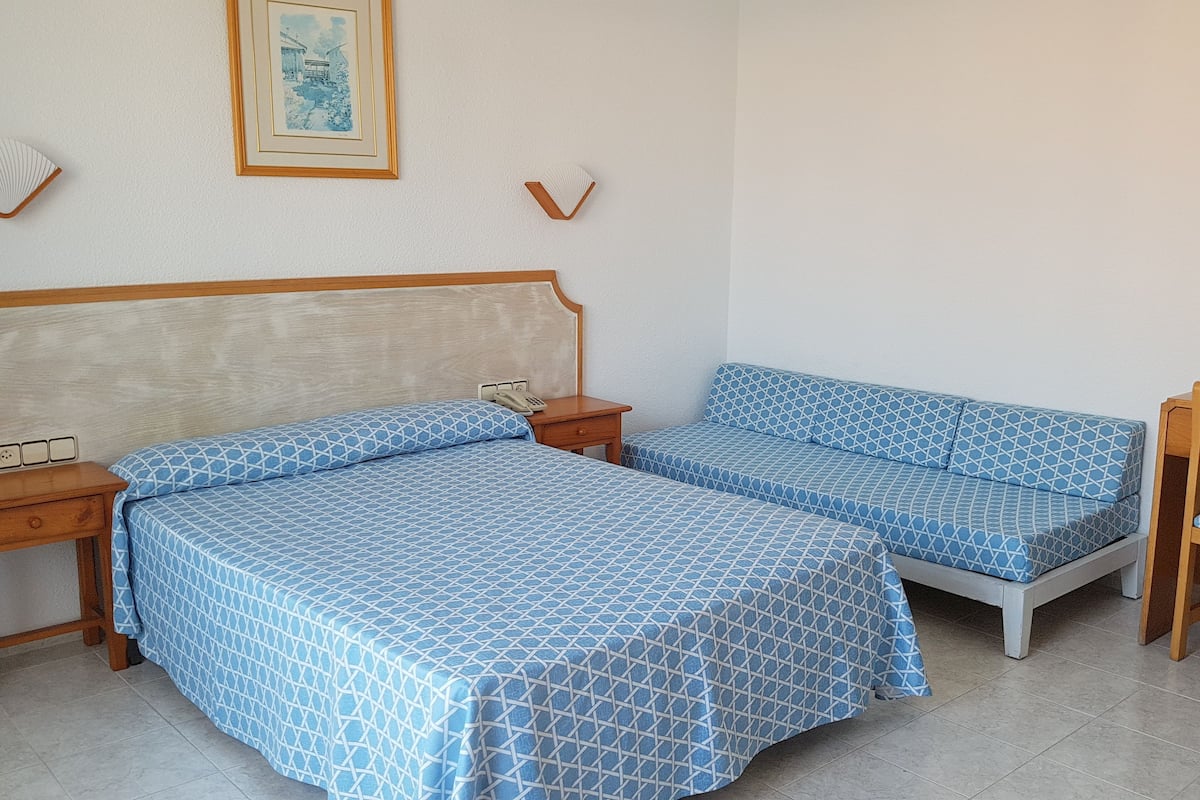 Een slaapkamer met twee bedden, een houten nachtkastje, een bijzettafeltje, een stoel en een spiegel.