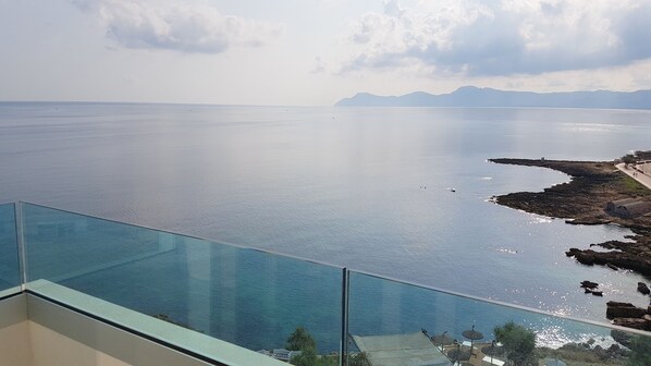 A panoramic view from a balcony overlooking a calm sea with distant mountains, a rocky shoreline, and a clear sky. - Apartamentos Stil Mar y Paz (Santa Margalida)