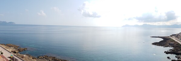 Vista costera con cielo despejado, mar tranquilo, costa rocosa y un paseo pavimentado a lo largo de la costa.