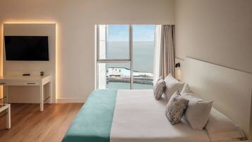 Una habitación de hotel con cama, escritorio, televisión y vista al mar.