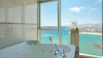 Un baño con un ventanal grande, una bañera y vistas a la playa y al océano.