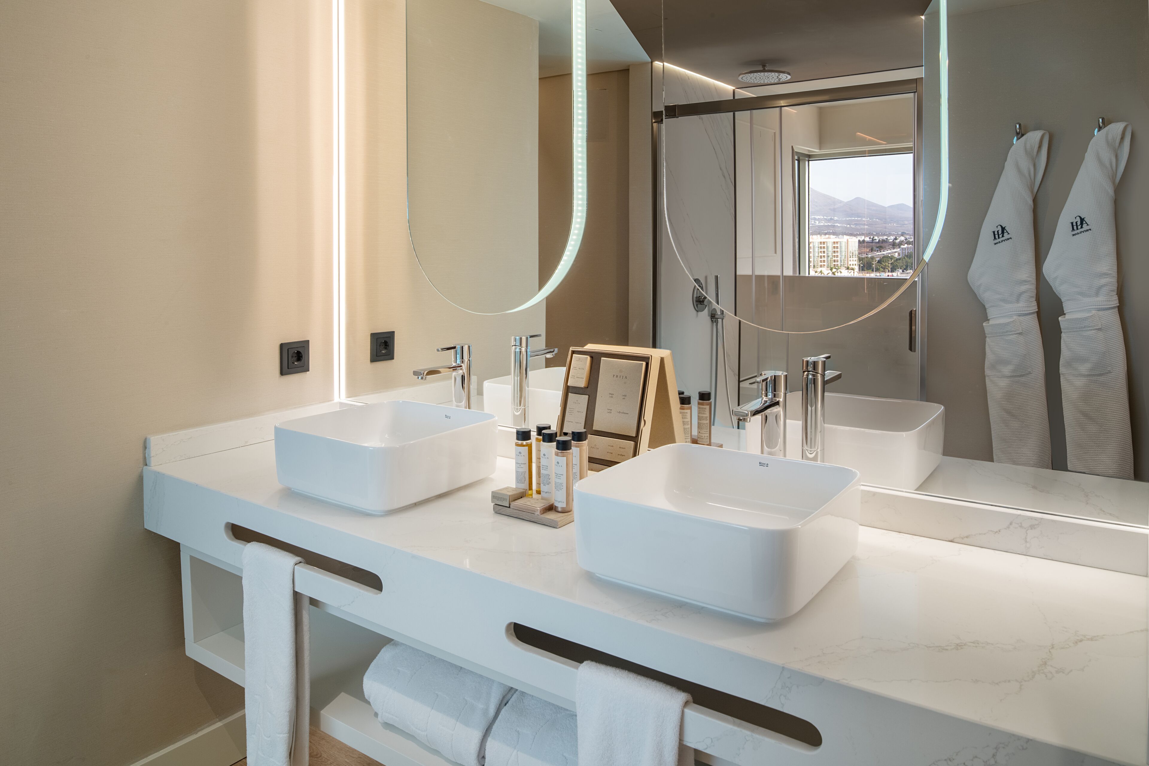 A modern bathroom with two large white sinks, a large mirror, and a view of a cityscape through a window.