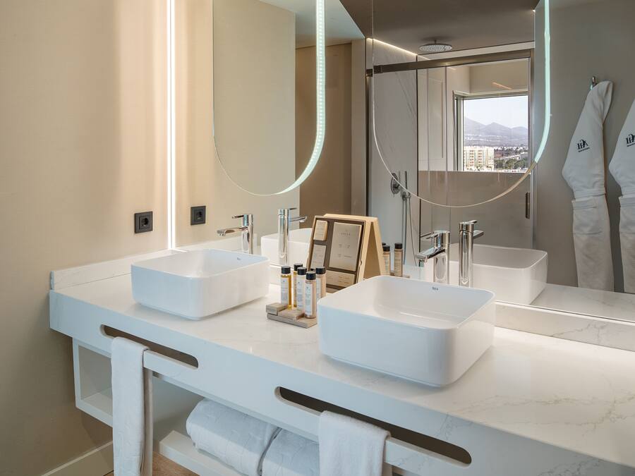 A modern bathroom with two large white sinks, a large mirror, and a view of a cityscape through a window.