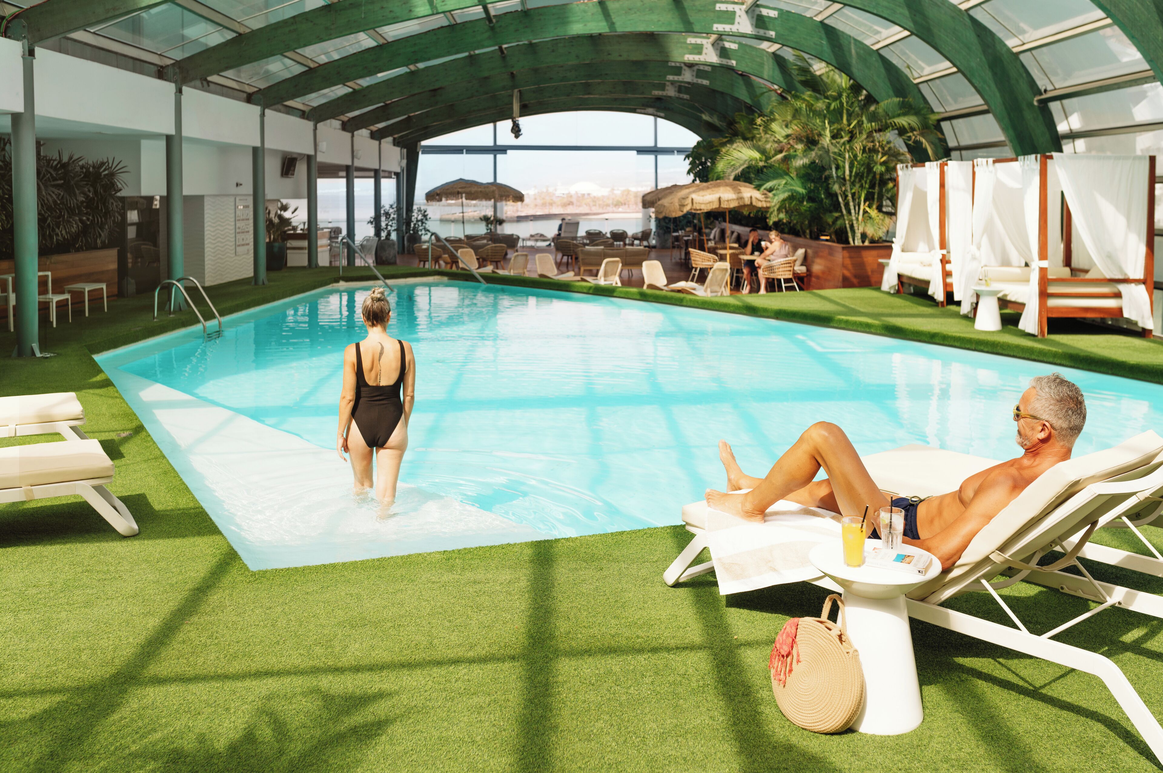 Une piscine intérieure dotée d’un revêtement de gazon synthétique, de chaises longues et d’un espace abrité avec des parasols.