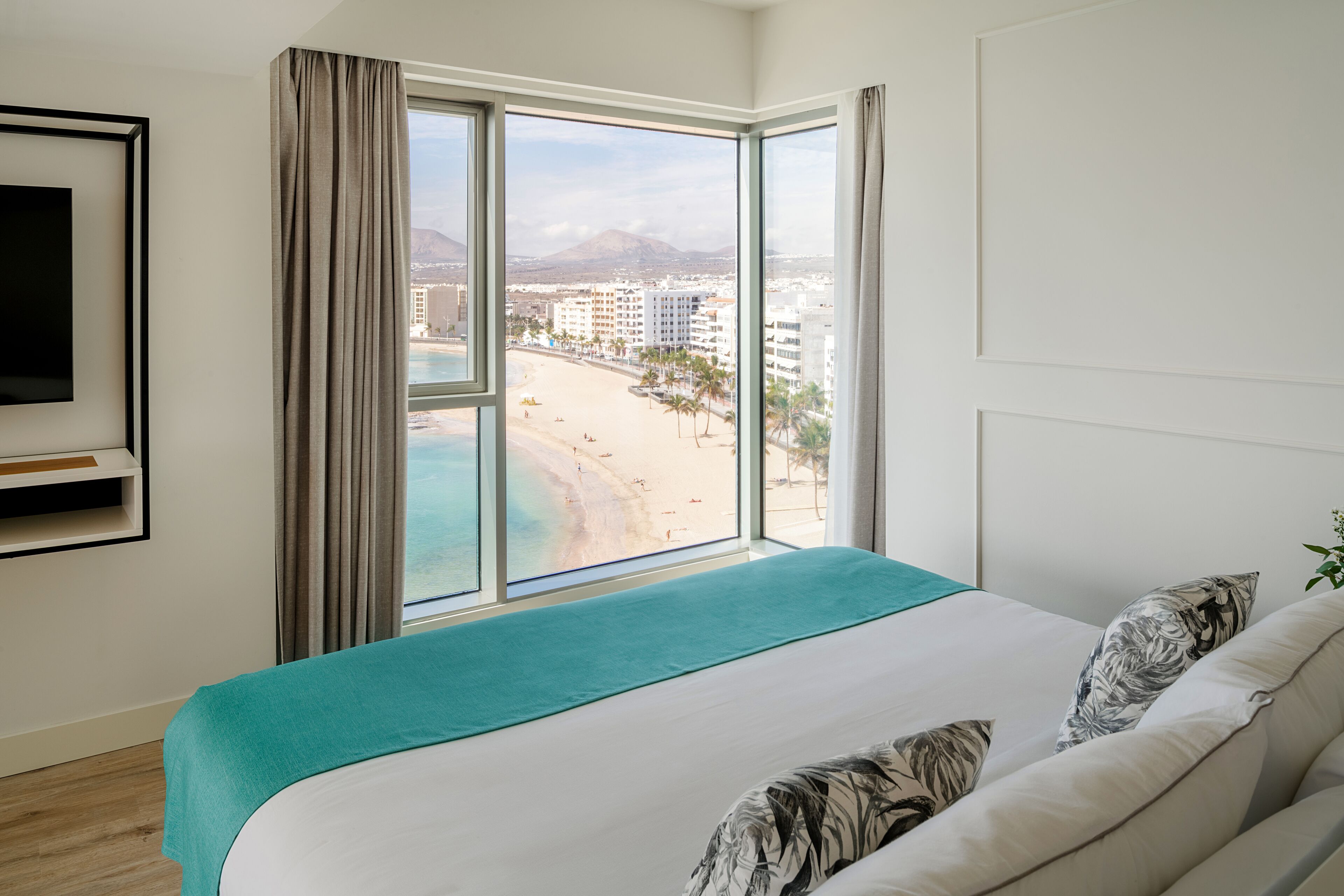 A hotel room with a large window offering a view of a beach and cityscape.