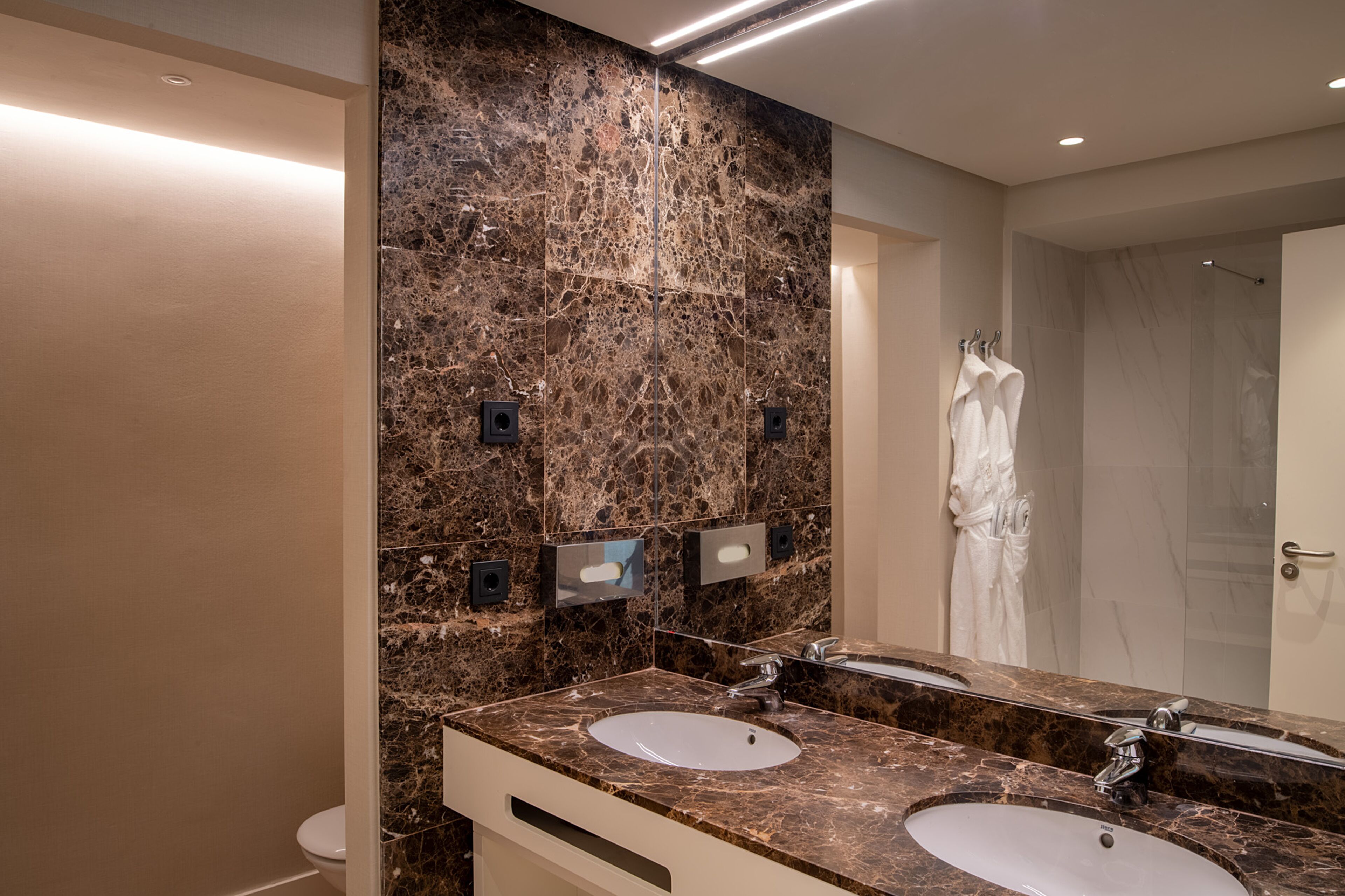 Un baño moderno con dos lavamanos, paredes de mármol y un espejo grande.
