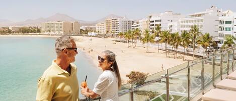 Un balcón con vista a una playa, palmeras y edificios de hotel.