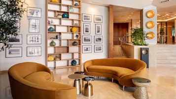 A modern lobby with a curved sofa, a wooden bookshelf, and framed pictures on the wall.