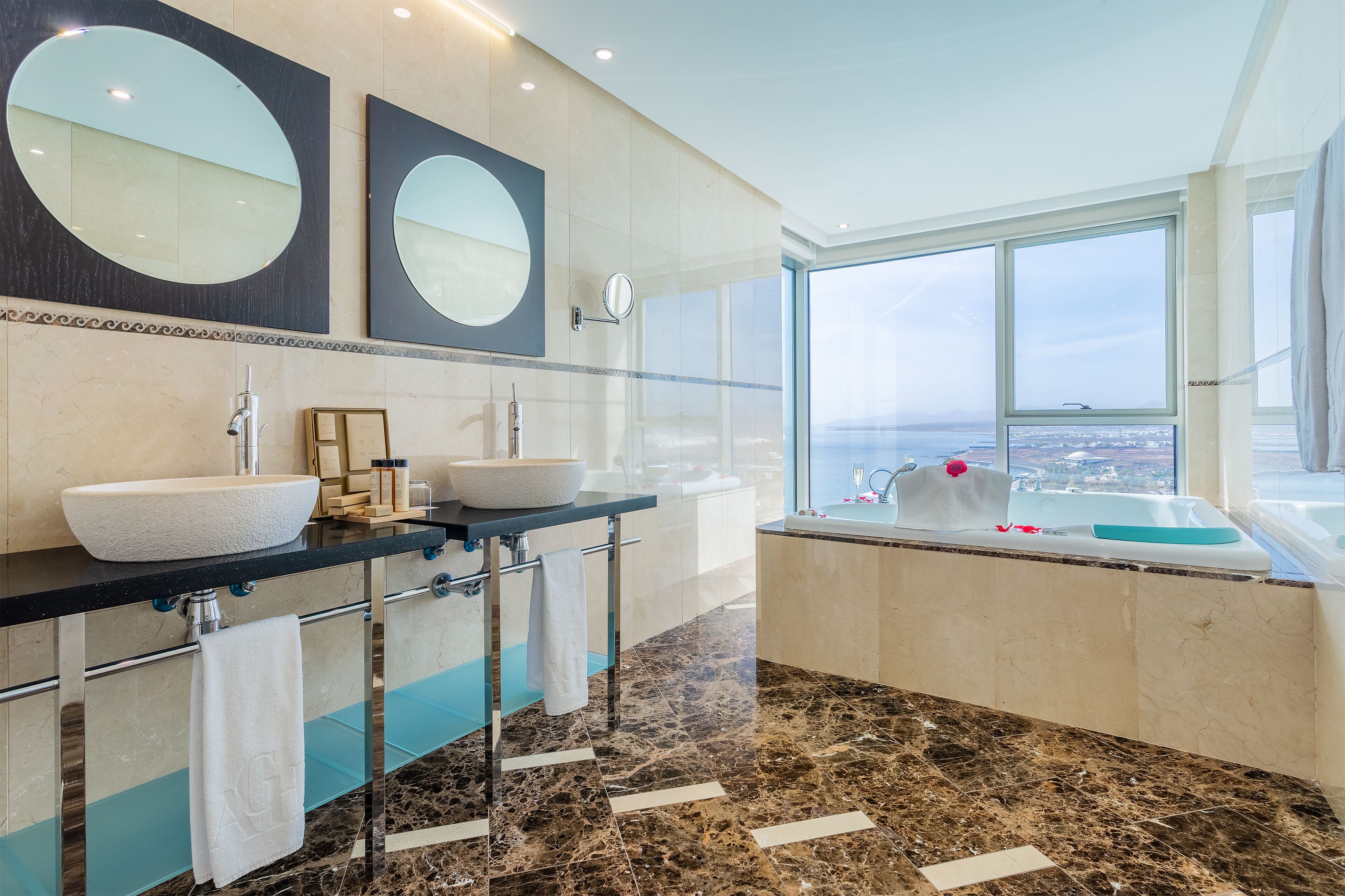 Un baño moderno con dos lavamanos, un espejo grande y una bañera con vistas.