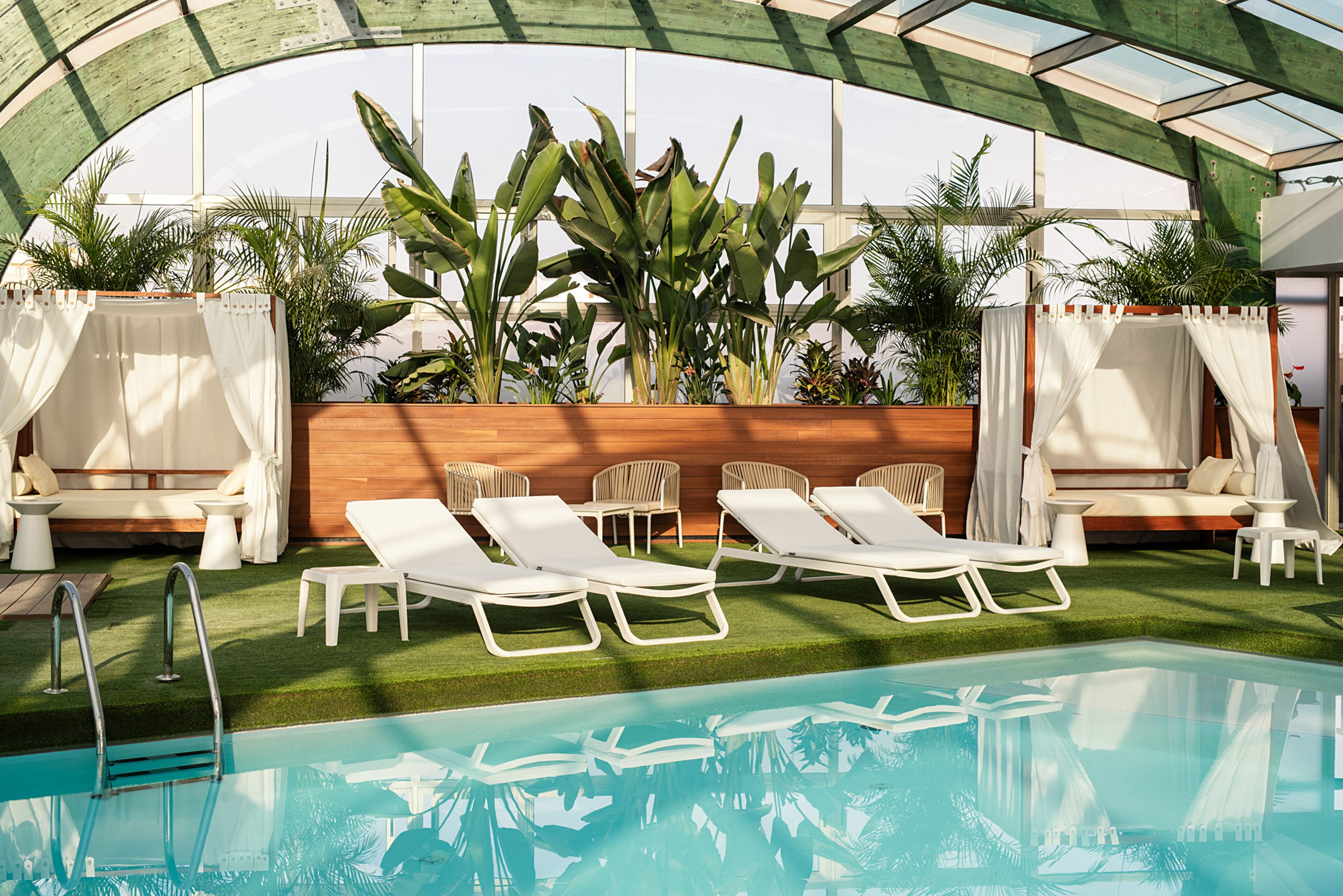 A pool area with lounge chairs, a wooden wall, and potted plants.