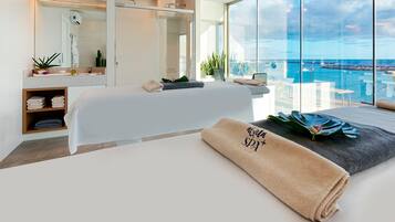 Un cuarto de spa con una camilla de masaje, un ventanal con vistas al mar y un estante con toallas.