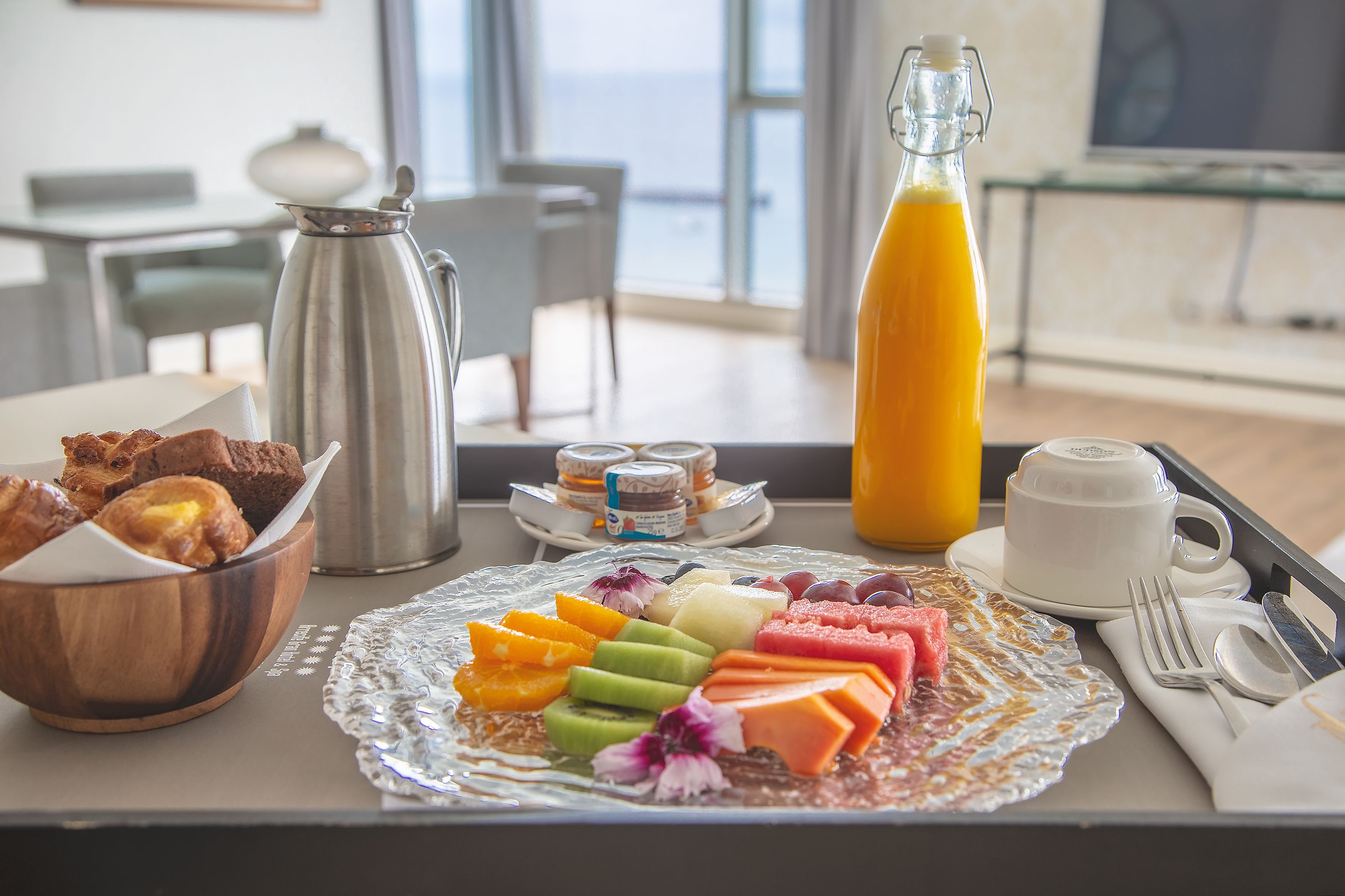 A breakfast tray with assorted pastries, fruits, and a glass of orange juice.